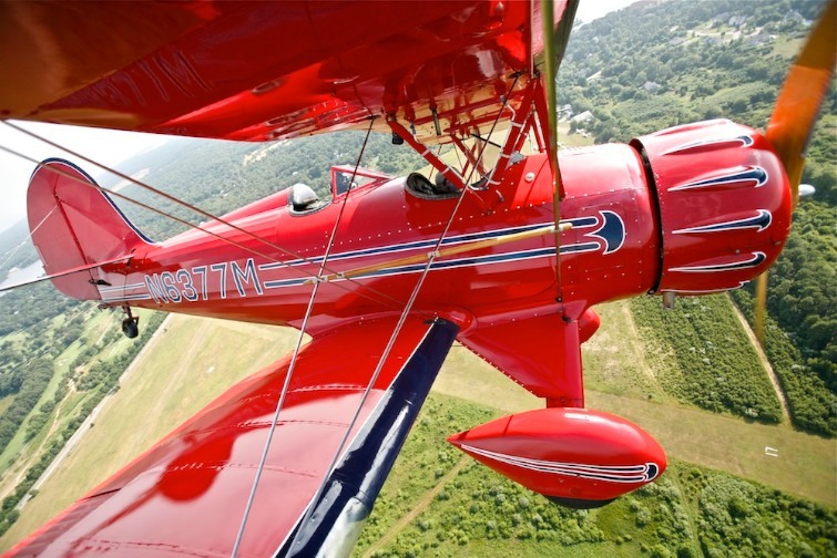 Red biplane flying over green fields